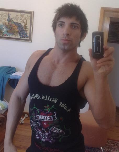 Aziz Shavershian wearing a black undershirt while holding a mobile phone in front of a mirror.