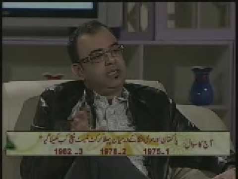 Azmi Haq during an interview and sitting on a couch, wearing eyeglasses, a black suit, and white long sleeves.