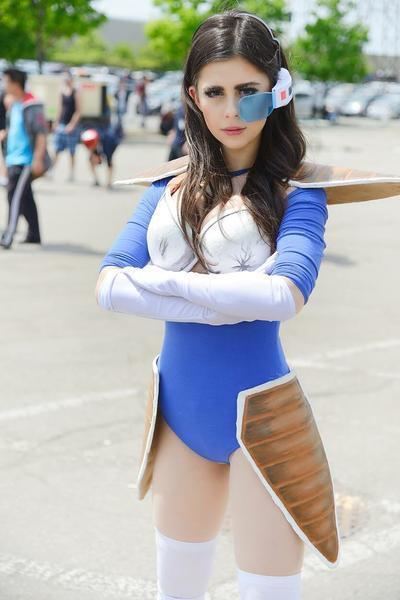 Azzyland with a serious face, with both hands, crossed under her chest, long hair, and wearing blue, white, with brown armor on her legs, a cosplay costume, and a blue, white, and red eyepiece and white knee socks of a character called Vegeta from an acclaimed Japanese anime series ‘Dragon Ball Z’.