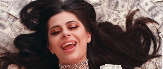 Azzyland laughing while lying on a pile of money, with long black hair, and wearing a fancy silver necklace.