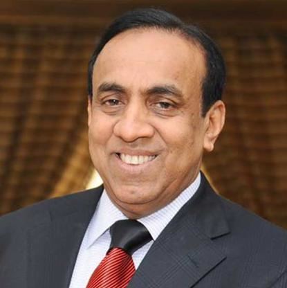 B. Ravi Pillai smiling while wearing a black coat, white long sleeves, and red necktie