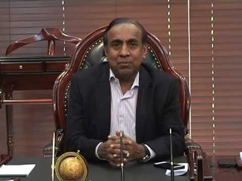 B. Ravi Pillai smiling while his hands together and wearing a black coat and striped long sleeves