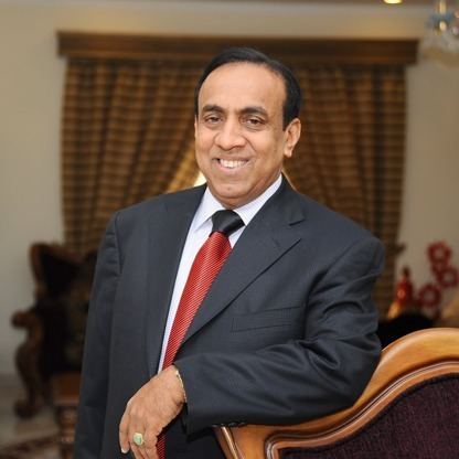 B. Ravi Pillai smiling while wearing a black coat, white long sleeves, and red necktie