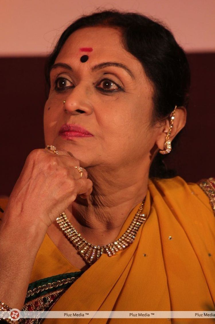 B. Saroja Devi's hand on her chin while wearing a yellow dress and some pieces of gold jewelry
