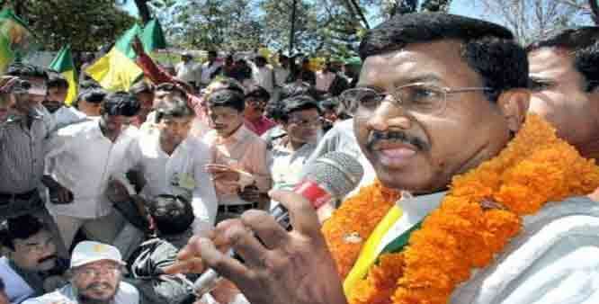 Babulal Marandi, Former Chief Minister of Jharkhand is serious, mouth half open, the tongue is visible, has black hair and a mustache, left and right hand holds a microphone, wears eyeglasses, orange white long sleeves under an orange garland. He is surrounded by a lot of men.