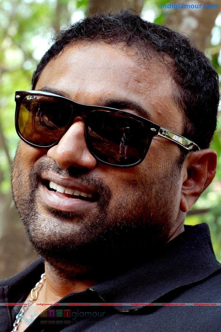 Baburaj smiling while wearing shades and black polo shirt