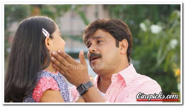 Baby Niveditha with black hair and wearing hairpin while looking at Gopalakrishnan Padmanabhan with a mustache and wearing a pink polo shirt in a movie scene from Moz & Cat (2009 film).
