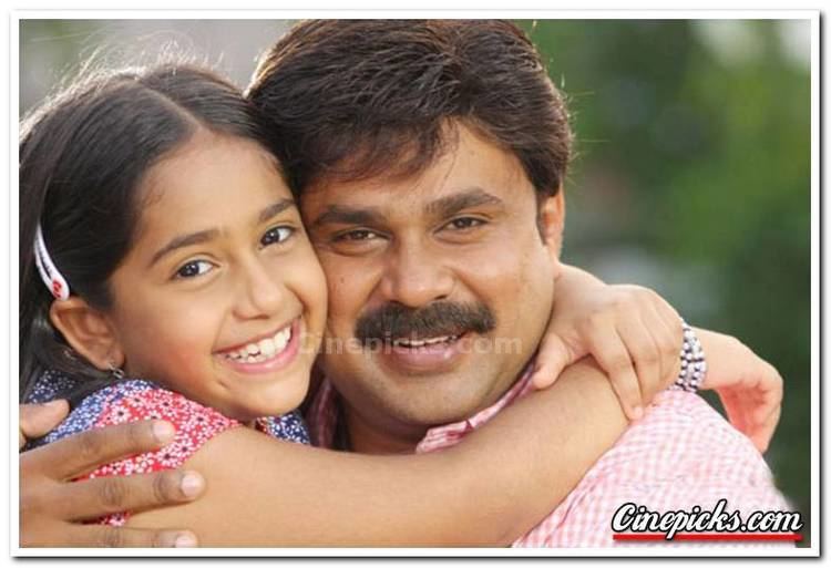 Niveditha Vijayan aka Baby Niveditha, a Malayalam child actress, smiling, hugging with Gopalakrishnan Padmanabhan better known by his stage name Dileep, smiling, with a mustache and wearing a pink polo shirt.