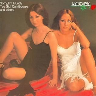 Cover art for the album by Baccara, while they are sitting on the floor with red cloth, and Mayte is wearing a black dress and María is wearing a white dress