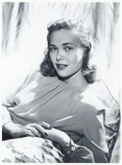 Barbara Daly Baekeland smiling while sitting on a couch and wearing a blouse and wristwatch