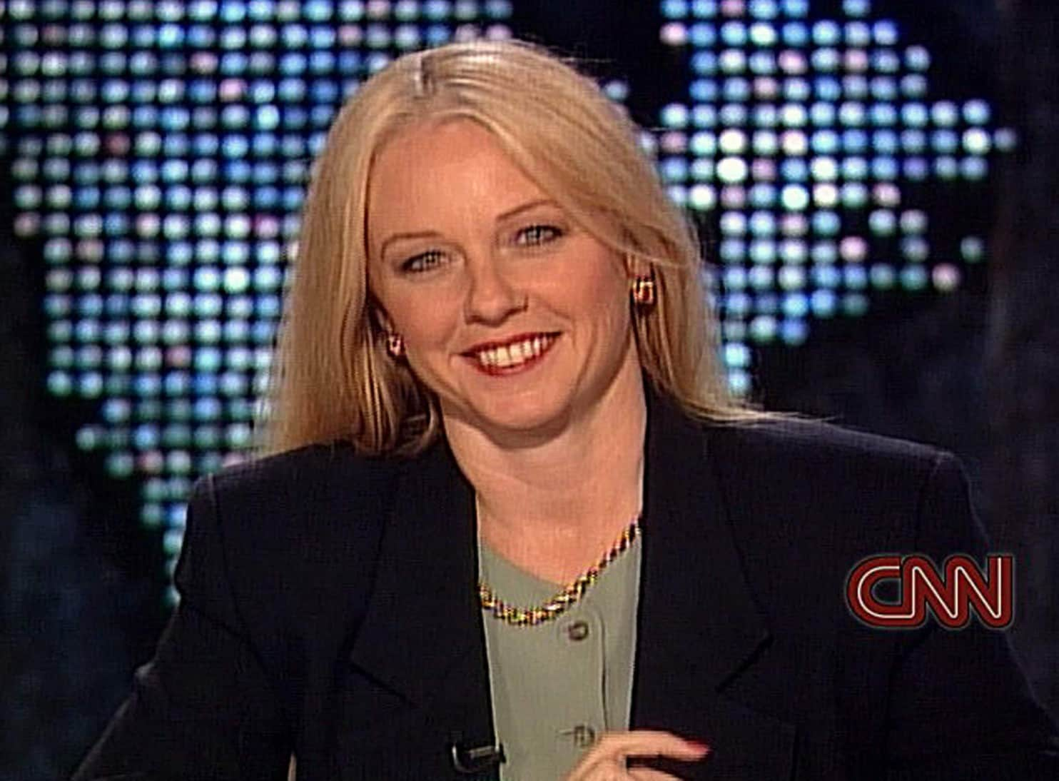 Barbara Olson smiling while wearing a black coat, green inner blouse, earrings, and necklace