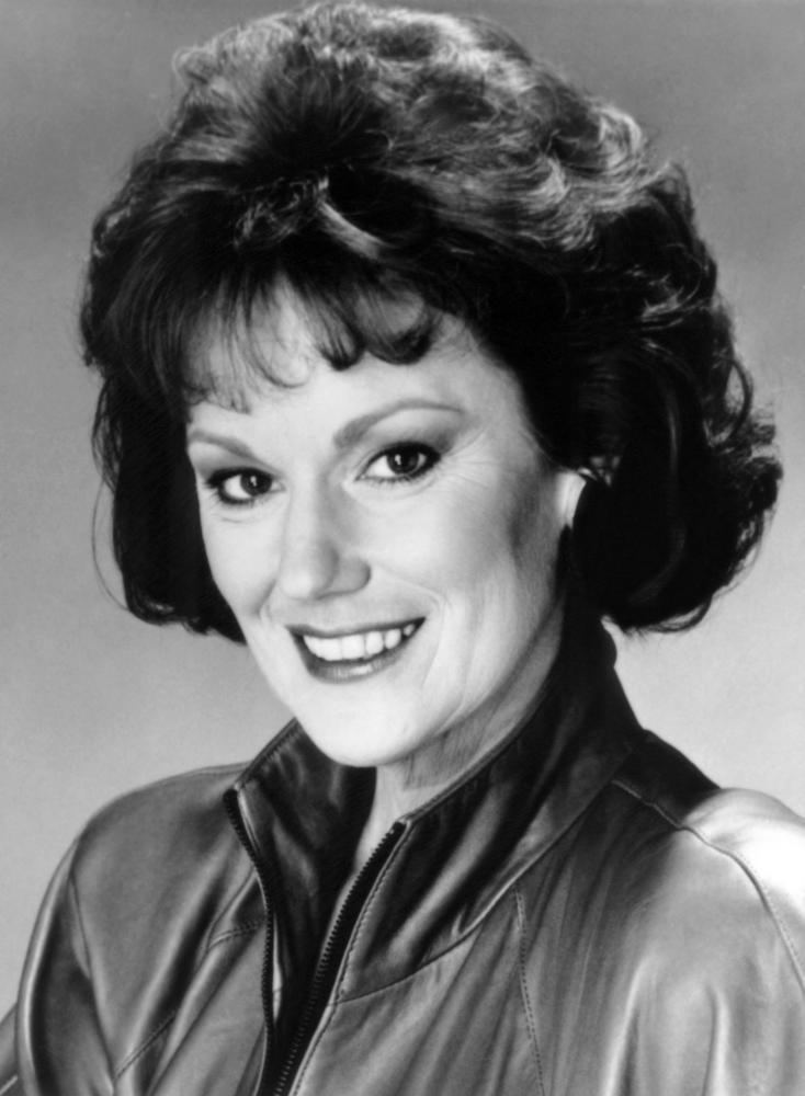 Barbara Rhoades smiling, with curly hair and wearing a leather jacket.