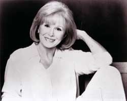 Barbara Stuart smiling and her arms leaning on her knees while wearing a blouse and pants