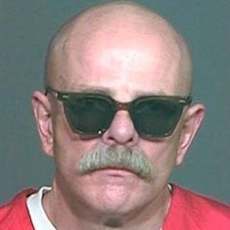 Barry Byron Mills looking serious with a mustache and a bald head while wearing shades and a red shirt