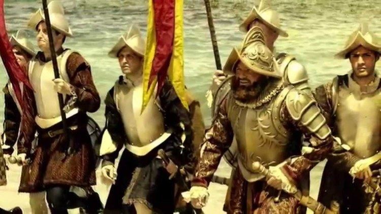 Reenactment of Ferdinand Magellan and his warriors arriving in the Philippines. They are holding their swords and flag while wearing motion helmets, brown skirts, and brown long sleeves under a gold body armor