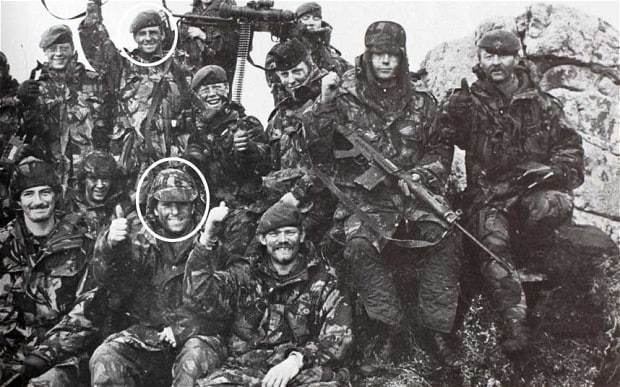In the Battle of Mount Tumbledown, A Group of British Army in black and white, on the top from left, is a man (1st) smiling, standing wearing beret with britting army uniform, next a man (2nd) smiling with white circle around his head, standing right hand up, left hand holding a rifle wearing a beret and British army uniform, (3rd) a man is standing, holding his rifle with his left hands wearing a beret and British army uniform, (4th) a man smiling, sitting, left hand thumbs up, wearing a beret and British army uniform, (5th) from left, a man is serious standing behind a machine gun, wearing a beret and British army uniform(6th) a man smiling, sitting hands down over his lap, wearing a beret and British army uniform, (7th) from left, a man smiling, sitting right hands up closed fist, while left hand holding the rifle, wearing a army cap and British army uniform, at the right is a man serious, sitting, right leg straight and left leg bend leaning to the large rock behind, right hands thumbs up, left hands on his pocket, has mustache wearing a beret and British army uniform, at the bottom from left, is a man smiling, sitting on the ground, has mustache, wearing a beret and British army uniform, (2nd) from left, a man smiling, sitting behind, wearing a beret and British army uniform, (3rd) from left, a man smiling, sitting on the ground, right hand thumbs up, left hand over his lap, wearing a beret and British army uniform, (4th) a man smiling, sitting on the ground, right hand up thumbs up, left hand over his lap, wearing a beret and British army uniform.