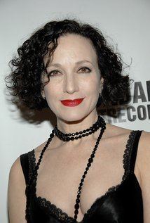Bebe Neuwirth smiling, with curly short black hair and wearing a necklace and a sexy black top.