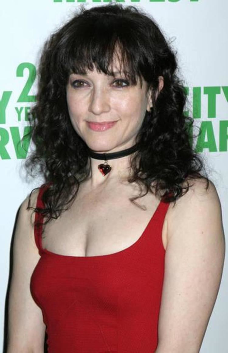 Bebe Neuwirth smiling, with curly black hair and wearing a choker and a red spaghetti top.