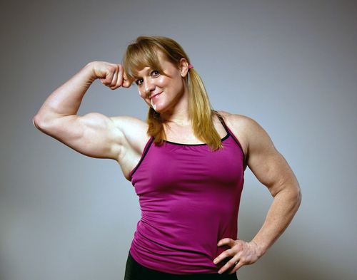Becca Swanson smiling while flexing her muscle and wearing a purple sleeveless top