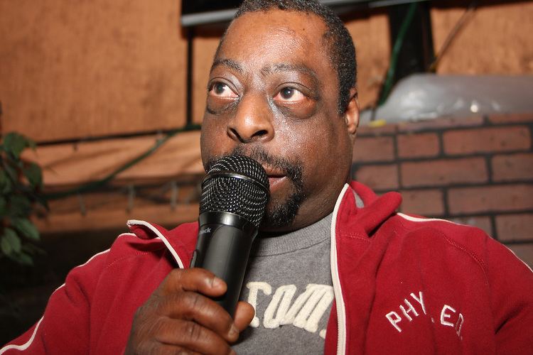 Beetlejuice wearing a red jacket, a gray shirt, and holding a microphone.