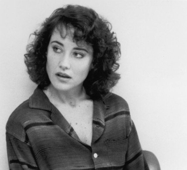 Belinda Bauer looking at the left side, with curly hair, while her mouth is open and she is wearing a long sleeve blouse