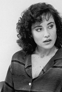 Belinda Bauer looking at the right side, with curly hair, while her mouth is open and she is wearing a long sleeve blouse