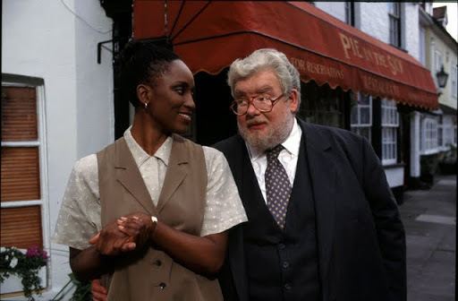 Bella Enahoro wearing a white polo and brown vest with an old man