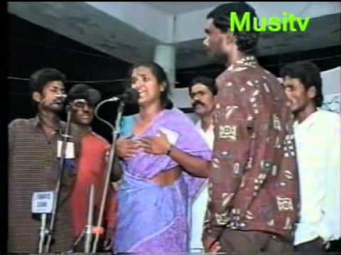 In the middle Belli Lalitha, an Indian Folk, is serious, speaking in the two standing microphones around her supporters, both hands on his chest, has black hair wearing a blue and purple Saree.
