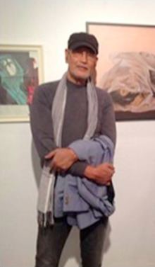 Benedicto Cabrera holding a blue jacket while wearing a black hat, eyeglasses, gray long sleeve, and gray scarf