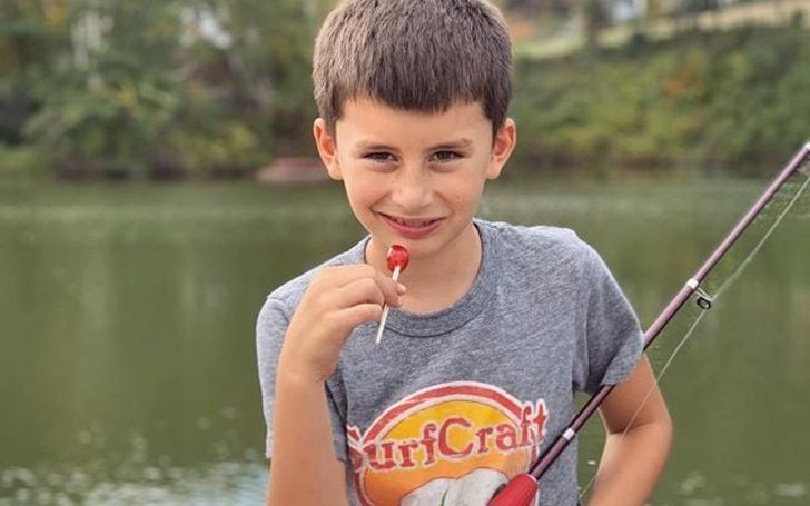 Benjamin Rein Brady smiling and holding a lollipop and Fishing rod while wearing a gray printed t-shirt