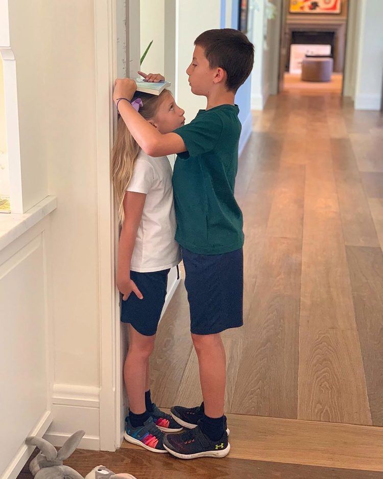 Benjamin Rein Brady measuring Vivian Lake Brady's height while he is wearing a green t-shirt, blue shorts, and rubber shoes
