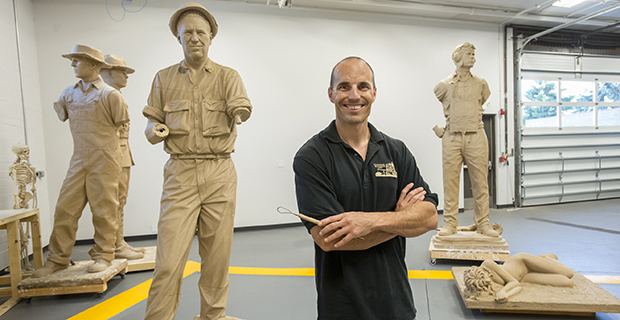 Benjamin Victor smiling with his sculptures at the back while wearing a black polo shirt