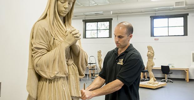 Benjamin Victor fixing his sculpture while wearing a black polo shirt