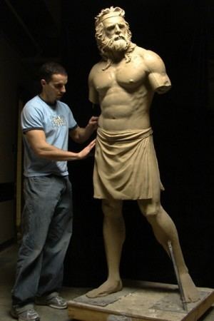 Benjamin Victor fixing his sculpture while wearing blue shirt and pants