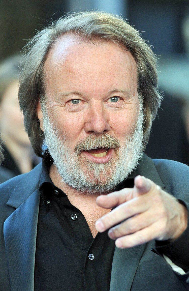 Benny Andersson pointing his finger while wearing a gray coat and black long sleeves