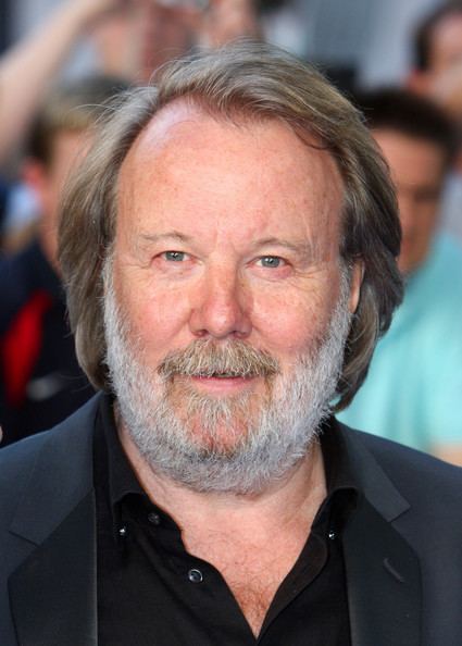 Benny Andersson smiling with mustache and beard while wearing a black coat and black long sleeves