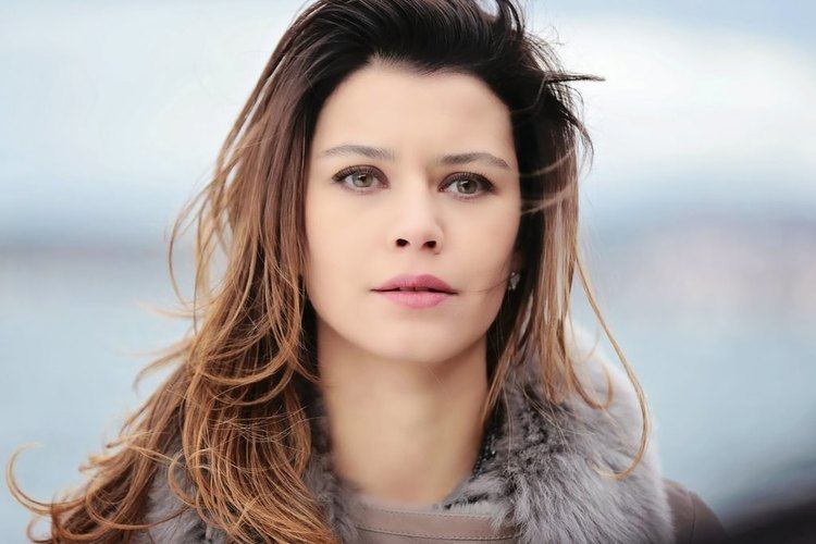 Beren Saat in a TV Show looking at something with light brown hair and wearing a furred coat.