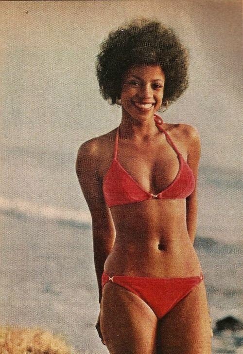 Bern Nadette Stanis with a big smile and kinky hair while wearing a red bikini and earrings
