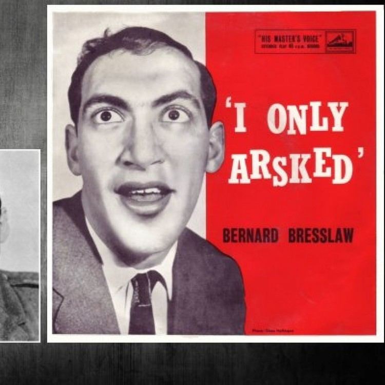 A poster with "I Only Arsked" on it featuring Bernard Bresslaw with a funny face while looking above, wearing a gray coat over white long sleeves, and a black necktie