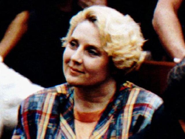 Betty Broderick wearing a checkered jacket and orange shirt with blonde hair.