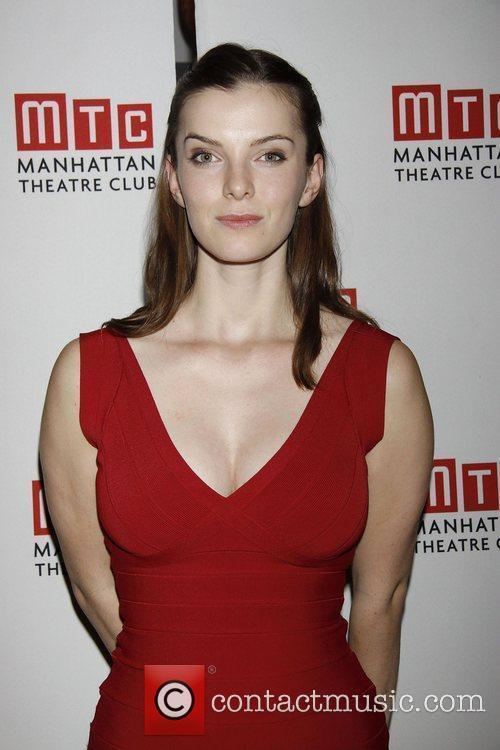 Betty Gilpin with a tight-lipped smile while wearing a red dress
