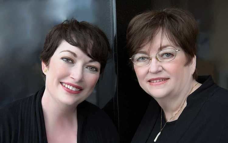 Mahtob and Betty Mahmoody are smiling. Mahtob with short hair and wearing a black coat while Betty wearing eyeglasses, a necklace, and a black blouse.