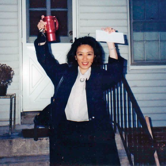 Betty Ong smiling and holding a tumbler and envelop while wearing a black jacket, white blouse, and black pants