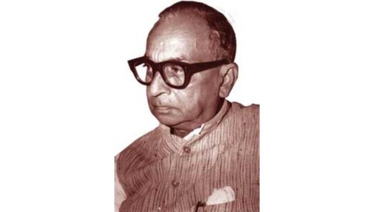 Bhagwati Charan Verma looking at something while wearing a striped polo and eyeglasses