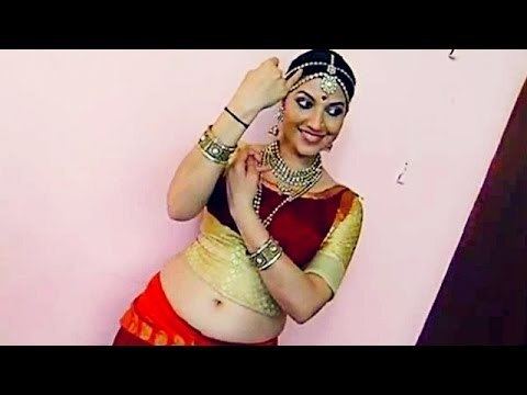 Bhavana Ramanna wearing a headdress, earrings, necklace, bracelets, a red and yellow top, and a red skirt.