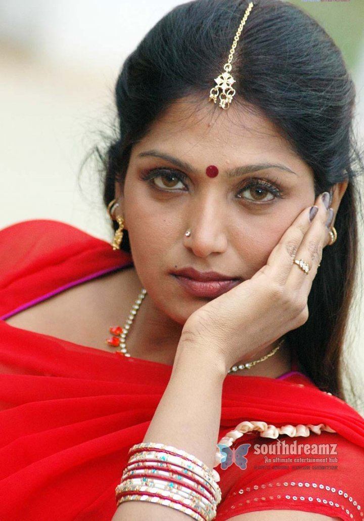 Bhuvaneswari hand on her face while wearing a red blouse and some pieces of jewelry