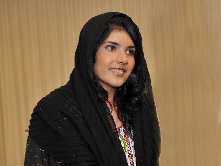 Bibi Aisha smiling while wearing a black hijab and a colorful dress