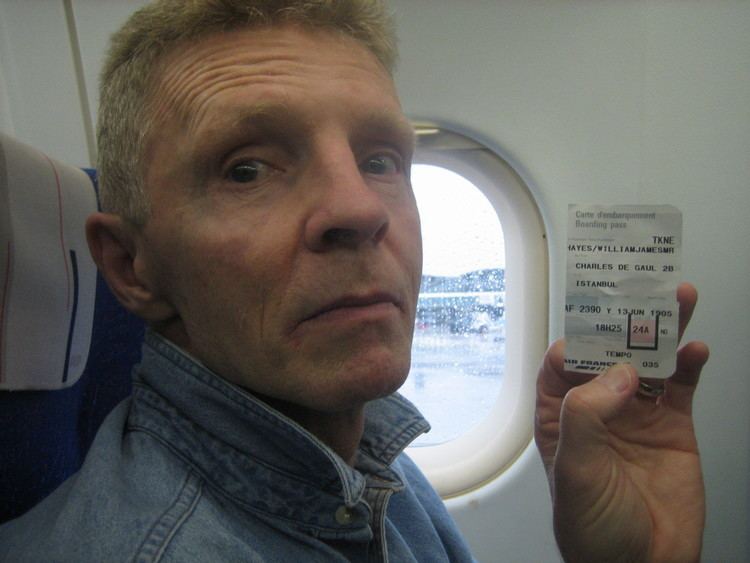 Billy Hayes showing a plane ticket while wearing a denim jacket