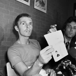 Billy Hayes showing his new passport while he is wearing a t-shirt