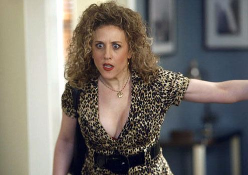 Bitty Schram with a shocked face while wearing a leopard print dress, black belt, and heart necklace